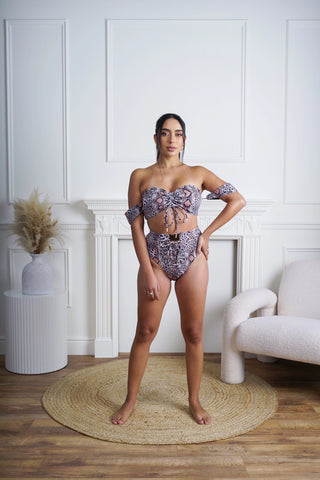 Woman wearing a leopard patterned bikini set in a stylish room with white walls and wooden floor.